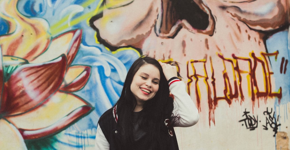 woman wearing black and white letterman jacket standing in front of mural painting