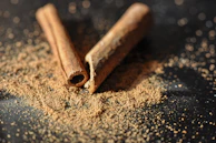 Close-up of cinnamon powder spilling gently from a wooden scoop onto a rustic surface.