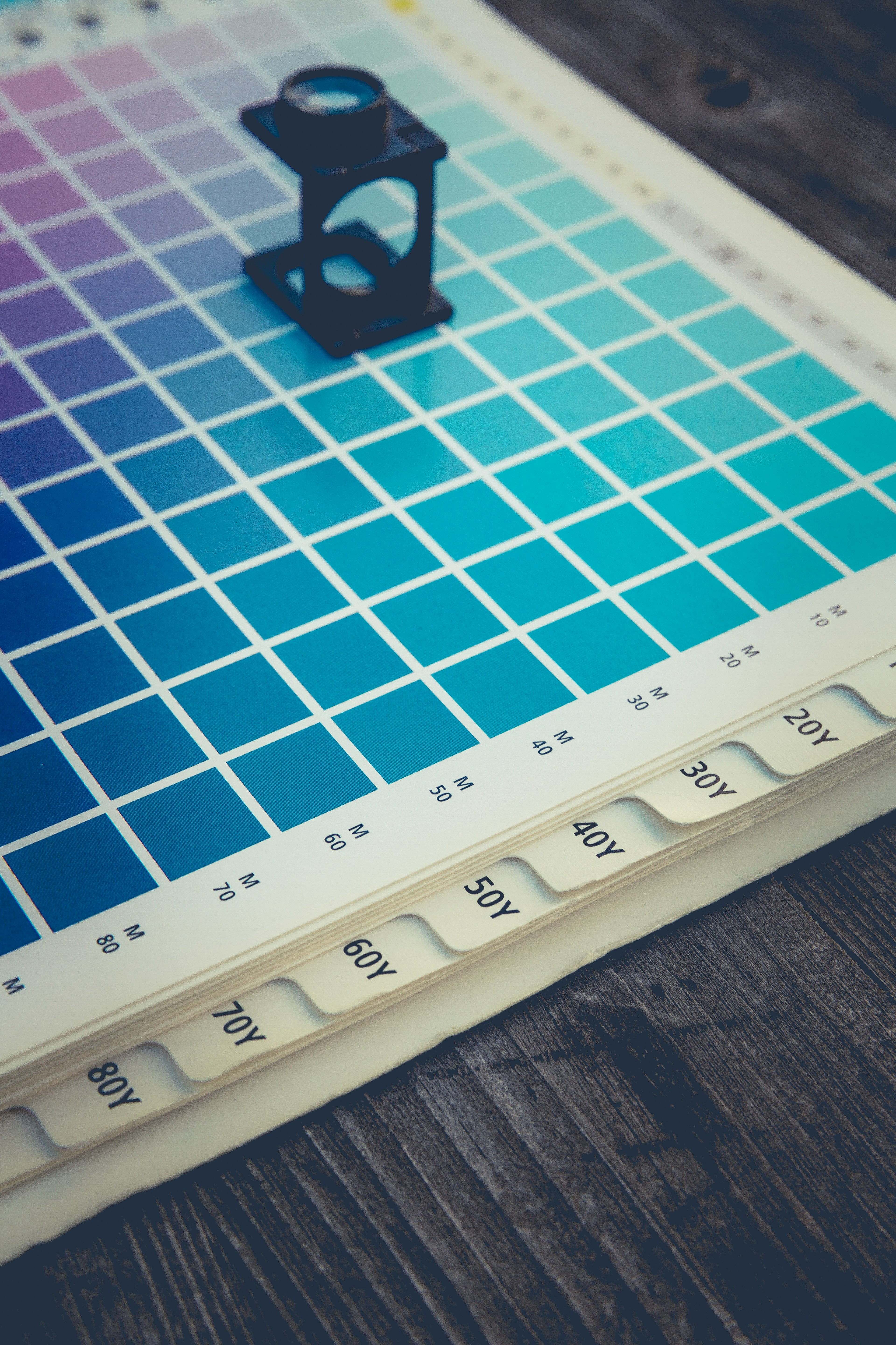 Lupa de impressão apoiada sobre um catálogo físico de cores em tons azuis.