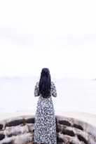 woman wearing black and white long sleeve dress standing facing sea during daytime