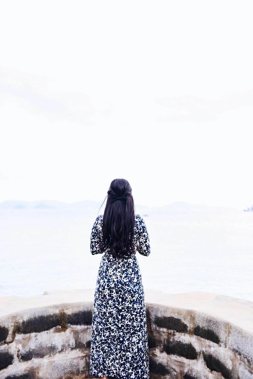 昼間、海に面して立っている黒と白の長袖ドレスを着た女性