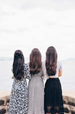 three woman looking back and facing body of water