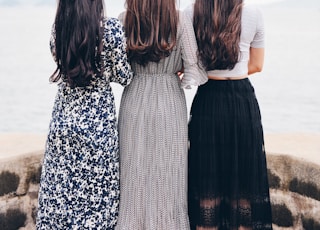 three woman looking back and facing body of water