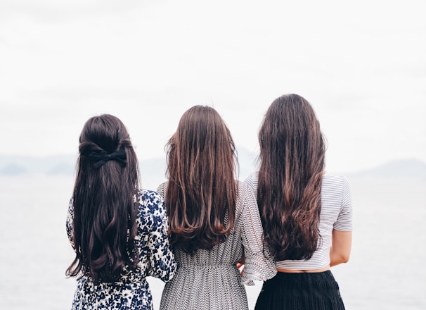 three woman looking back and facing body of water