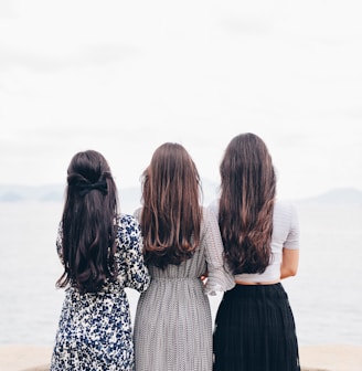 three woman looking back and facing body of water