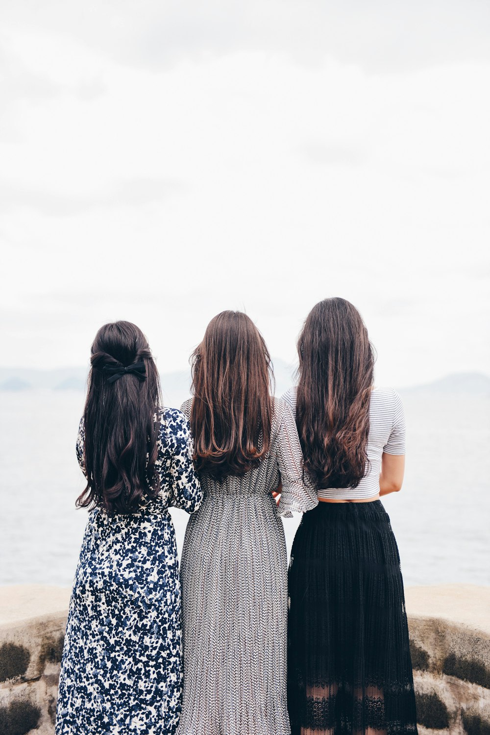three woman looking back and facing body of water