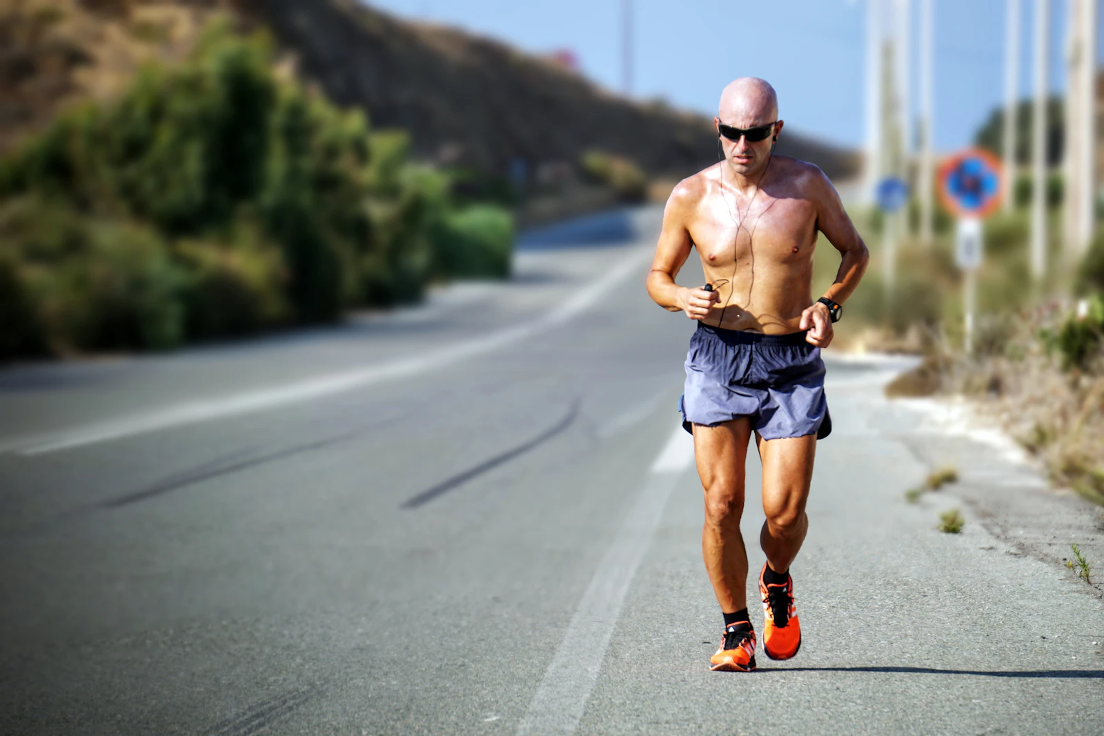 Mature man jogging on a sunlit road with earphones.