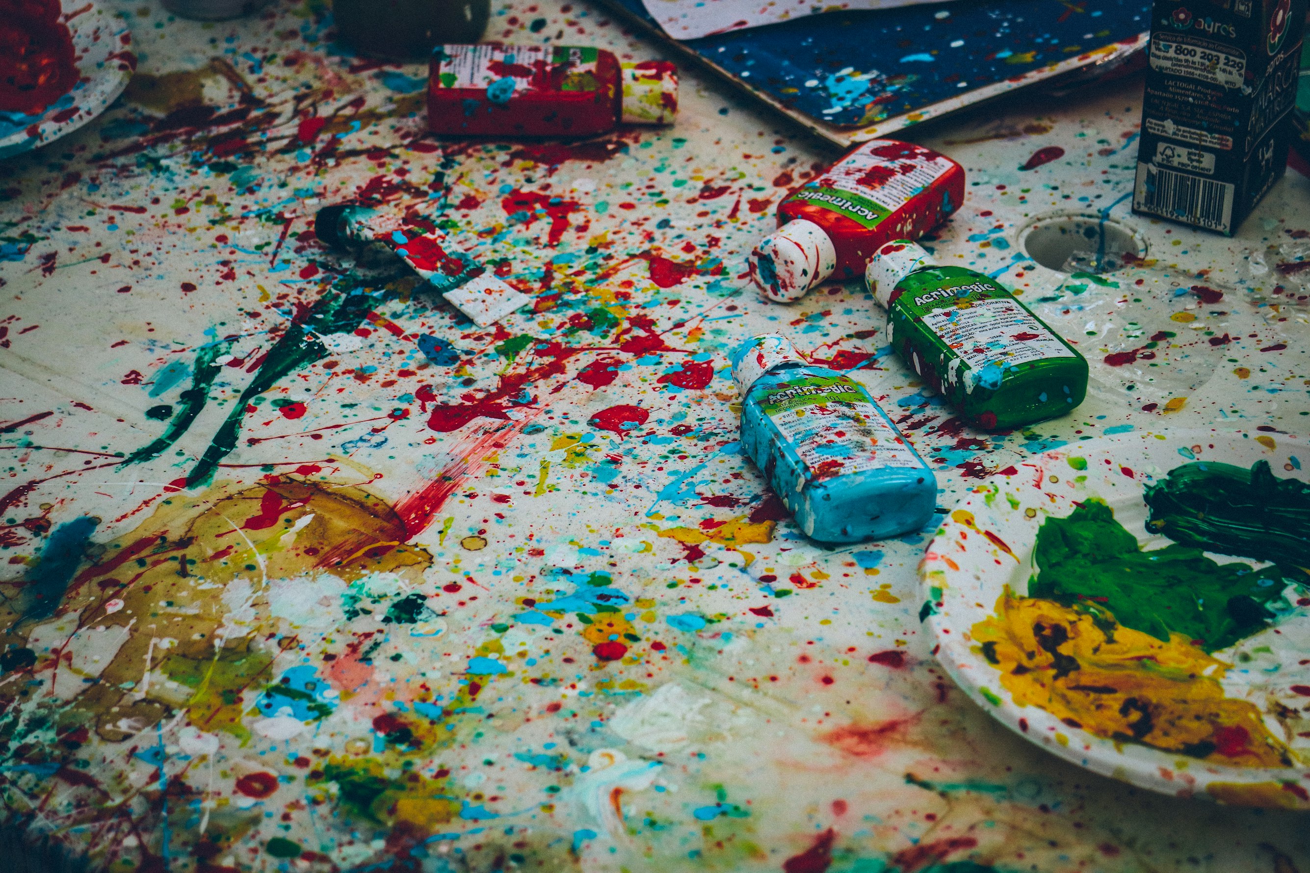 Assorted colored paint bottles on top of floor covered in splattered paint. Photo by Ricardo Viana