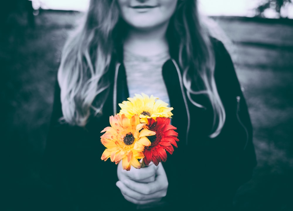 selective-color photo of person holding yellow and red flowers