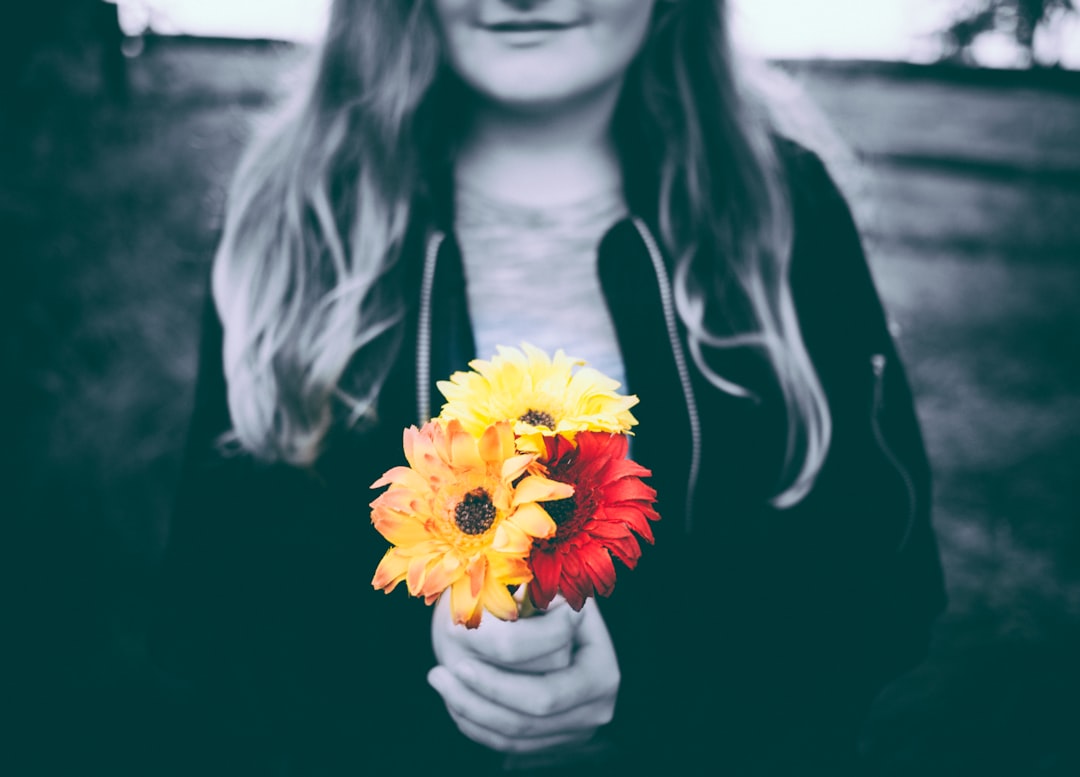 selective-color photo of person holding yellow and red flowers