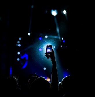 low light photography of person raising hand holding smartphone