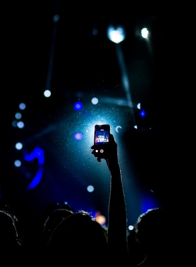 low light photography of person raising hand holding smartphone