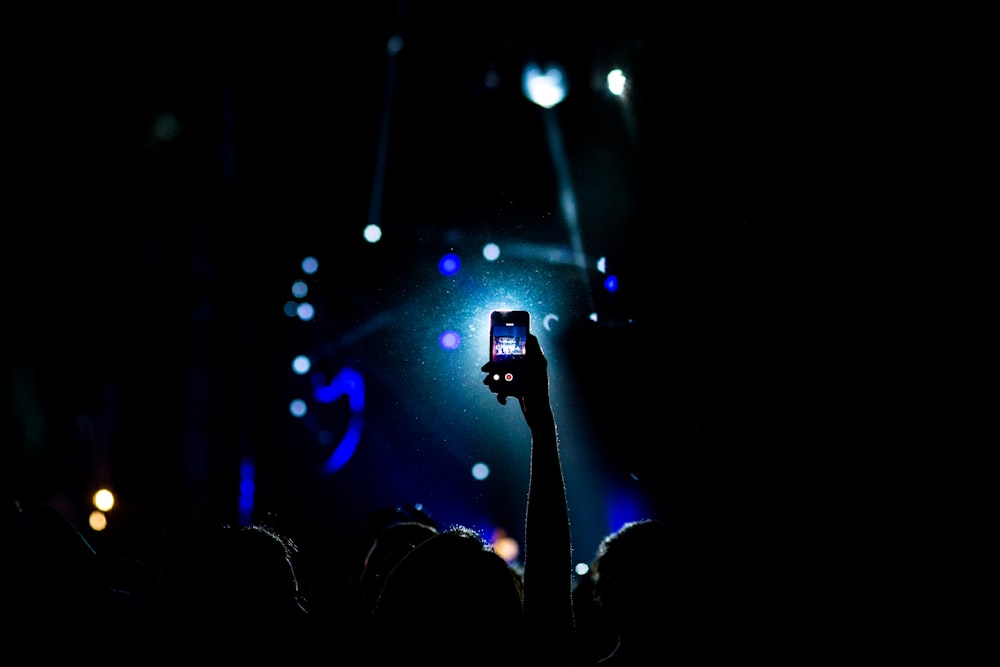 スマートフォンを手にした手を挙げている人の暗い場所での写真撮影