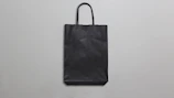Close-up of a sleek black paper bag with a minimalist white axora logo on a clean white background.
