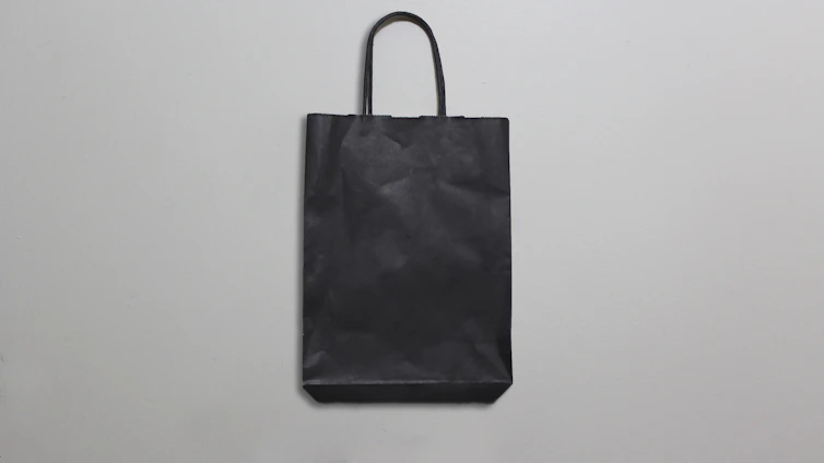 Close-up of a sleek, custom-printed paper bag resting on a minimalist white surface with soft natural light.