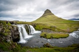 photo of waterfalls beside hill during cloudy daytime