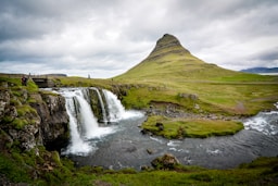 photo of waterfalls beside hill during cloudy daytime