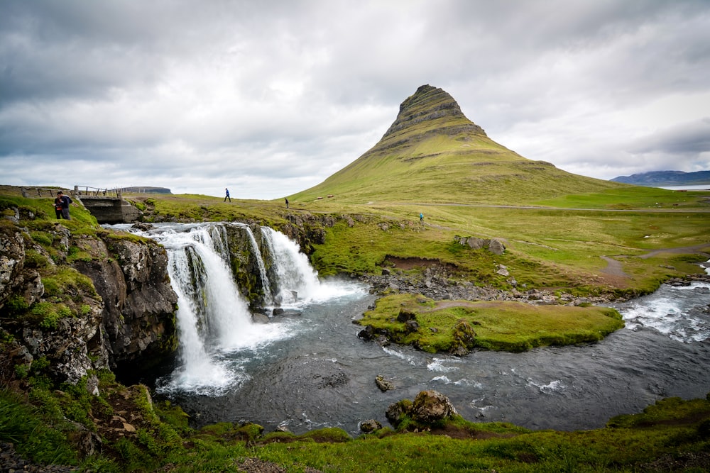 photo of waterfalls beside hill during cloudy daytime