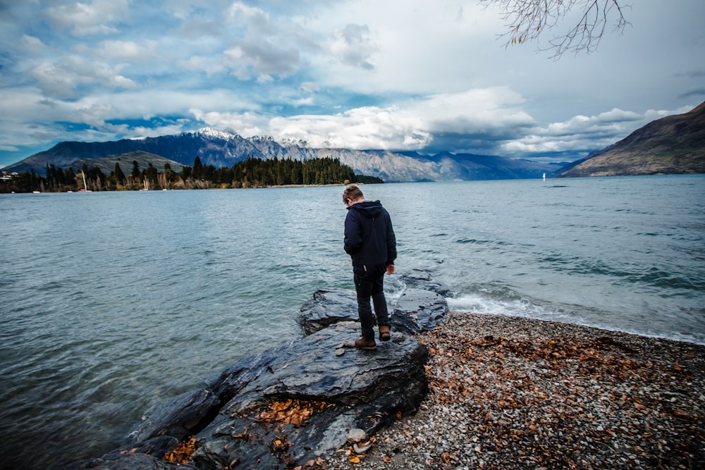 man standing on seashore under cloudy sky