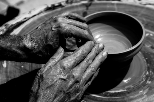 Two hands are skillfully shaping a clay pot on a pottery wheel, displaying the texture of the clay and the hands. The focus is on the intricate details of the potter's hands and the smooth surface of the clay vessel.