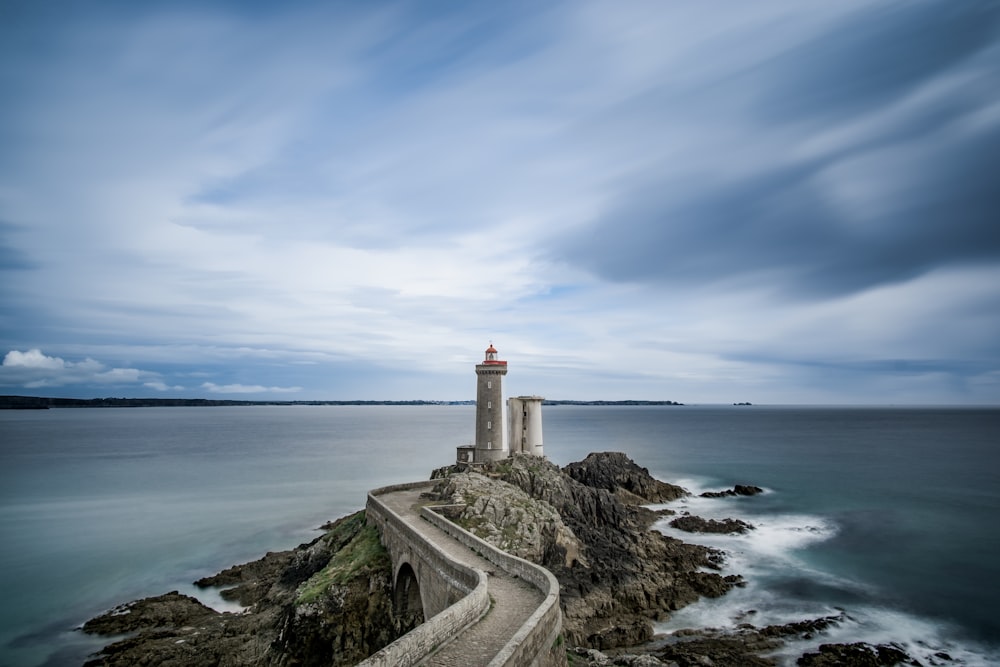 Phare en béton gris sur un plan d’eau entouré d’une falaise pendant la journée