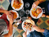 People eating burgers, fries, and roasted vegetables at a round table