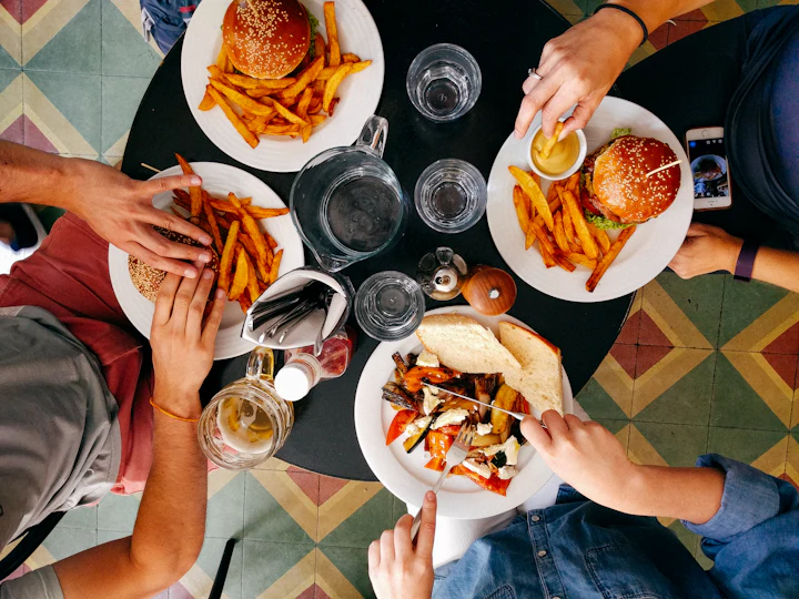 Friends reaching across a small table of plates and glasses on a patterned tiled floor