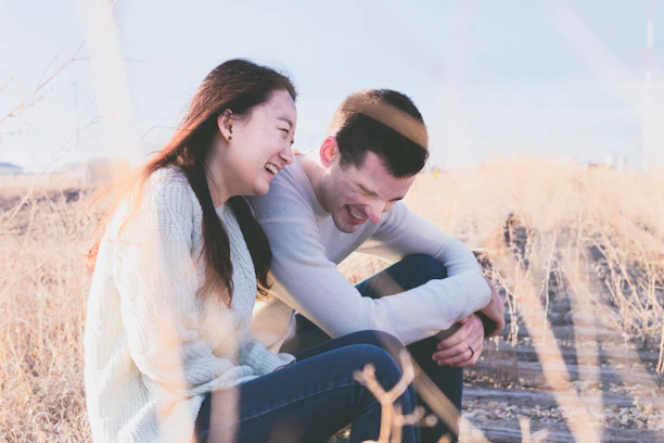 A sunlit candid photo of a couple laughing together in a terracotta-hued outdoor setting.