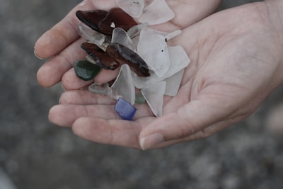 A collection of lavender and soft green sea glass scattered on a sunlit shoreline.
