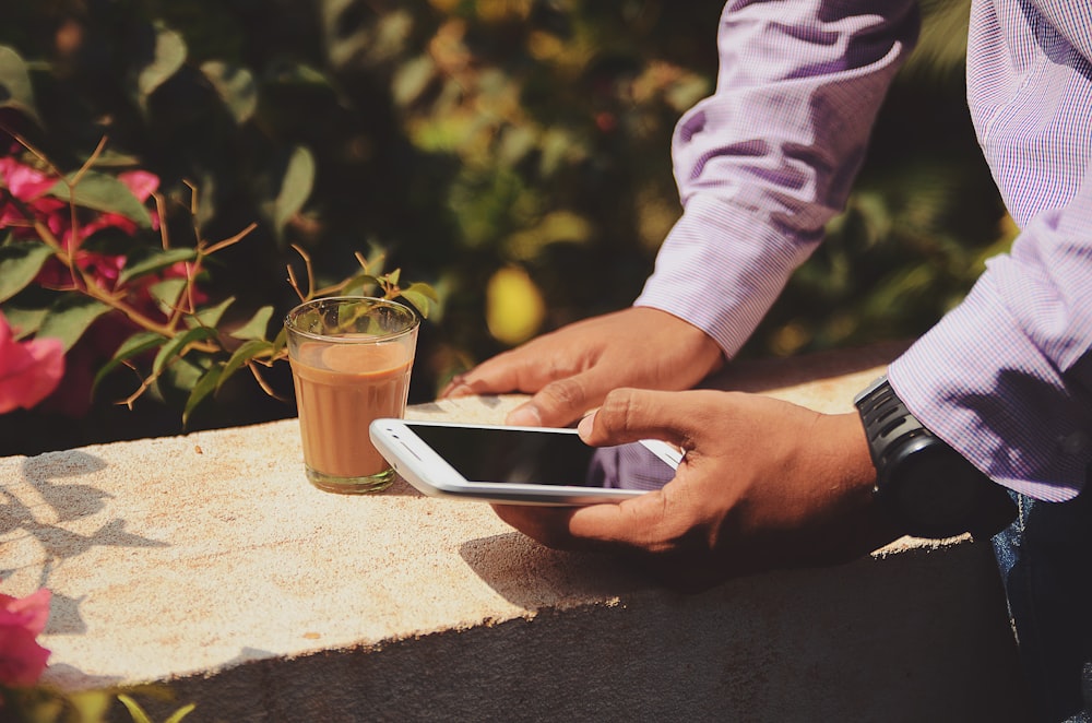 Hombre usando un teléfono inteligente al lado de un vaso para beber