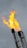 Bright orange flames are rising from the top of metal flare stacks against a cloudy gray sky.