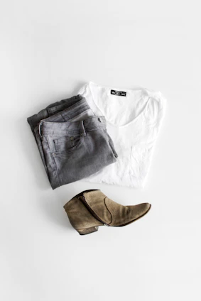 A pair of classic navy chinos casually folded with a leather belt on a soft blue background.