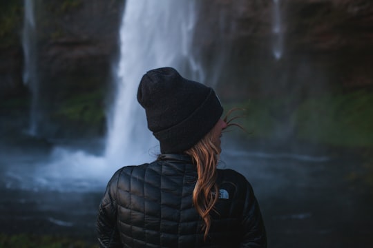 photo of woman wearing black jacket near waterfall in Seljalandsfoss Iceland