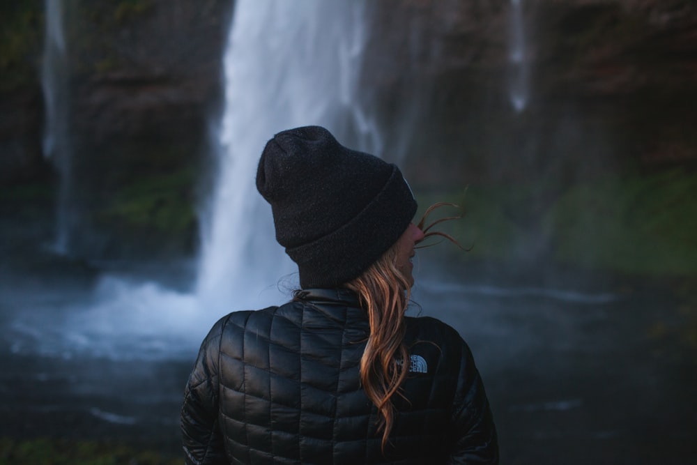 foto da mulher vestindo jaqueta preta perto da cachoeira