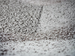 A close-up view of a textured surface with a thin crack running vertically through the middle. The surface appears to be rough and uneven, with small, granular particles spread across it.