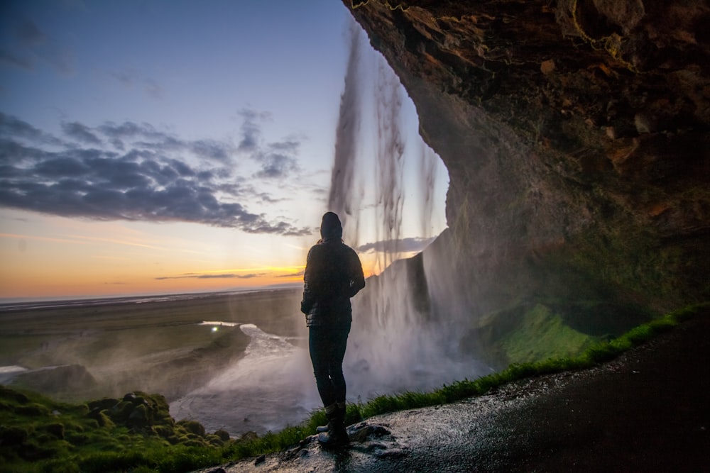 person standing under cave near waterfall