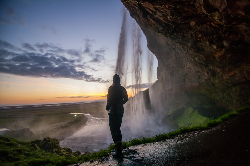 pessoa em pé sob a caverna perto da cachoeira