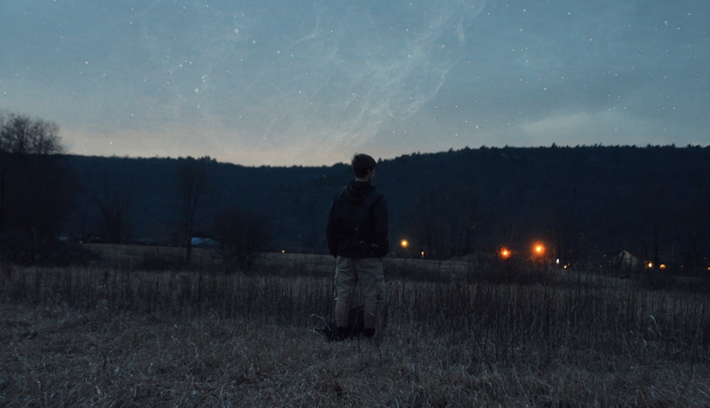 man wearing black jacket standing near grass looking at mountain