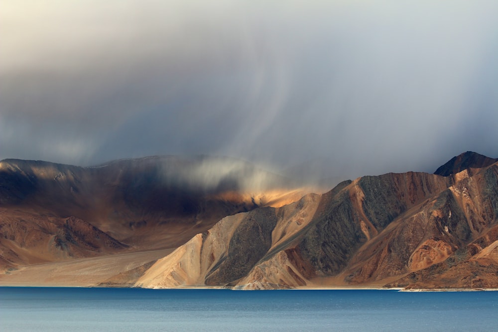 body of water and brown mountain under white sky at daytime