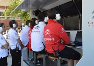 Several people wearing Citroën Racing uniforms and headphones are seated at a technical workstation with laptops and screens. They appear focused on monitoring or analyzing data.