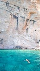 man floating over body of water near rock formation