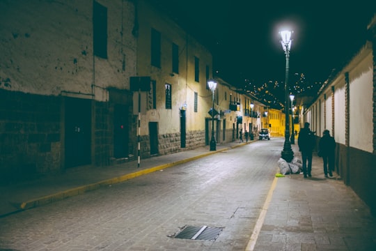 man in black jacket walking on sidewalk during night time in Cusco Peru