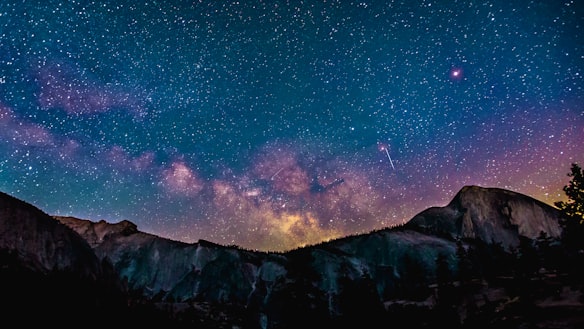 Dimly lit mountains give way to a starry night showing the Milky Way