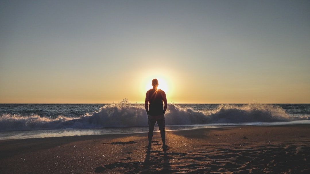 man in black shirt standing on beach during sunset