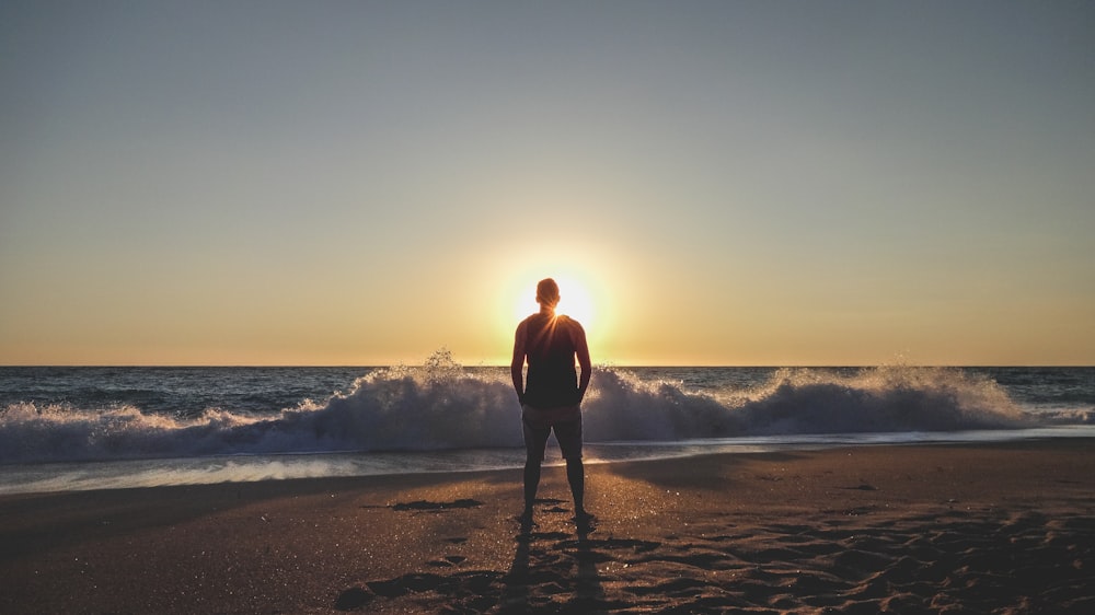 Homem de camisa preta em pé na praia durante o pôr do sol