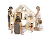 A group of children are engaged in play around a large, wooden dollhouse. The dollhouse is well-crafted with various rooms and pieces of furniture. Dolls are placed throughout, and the children appear to be interacting with the dolls and the house. The children are focused and seem to be enjoying their imaginative play. The scene is well-lit and the background is plain, enhancing the focus on the children and the dollhouse.