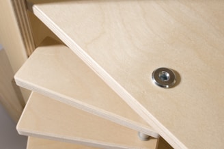 A close-up view of a wooden construction, likely a piece of furniture with multiple stacked shelves. A metal washer or fastener is embedded into the wood on the top shelf.