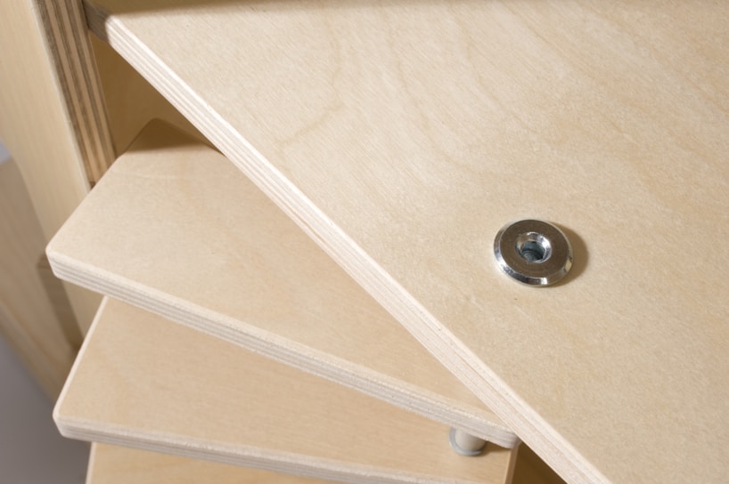 A close-up view of a wooden construction, likely a piece of furniture with multiple stacked shelves. A metal washer or fastener is embedded into the wood on the top shelf.