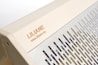 The image features a wooden structure with a carved name and website link engraved on the surface. Adjacent to the wooden area is a metallic section with evenly spaced vertical slits, providing a sleek and modern design.
