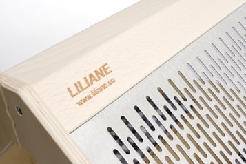 The image features a wooden structure with a carved name and website link engraved on the surface. Adjacent to the wooden area is a metallic section with evenly spaced vertical slits, providing a sleek and modern design.